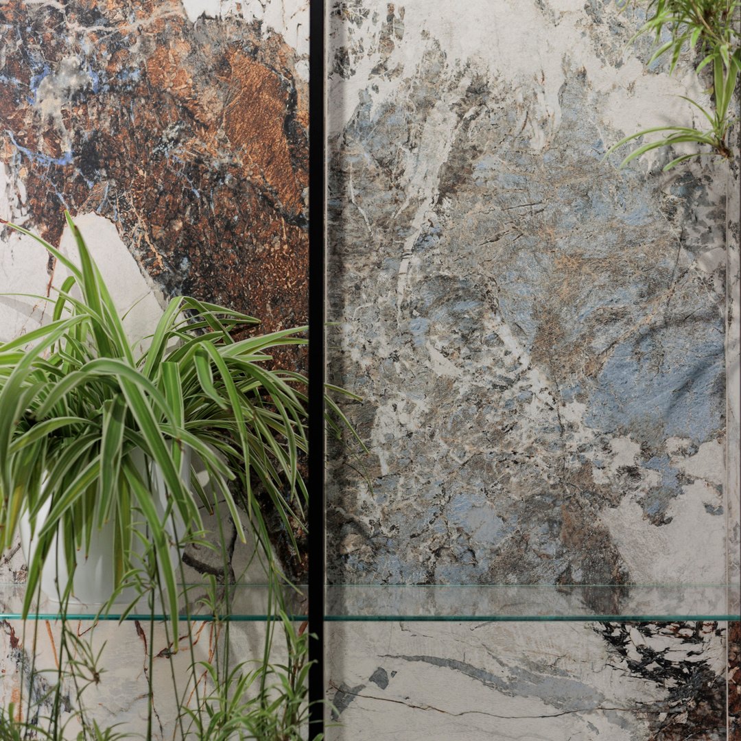 Wall with a plant with variegated white, grey, red, blue, and light blue marble-effect stoneware 